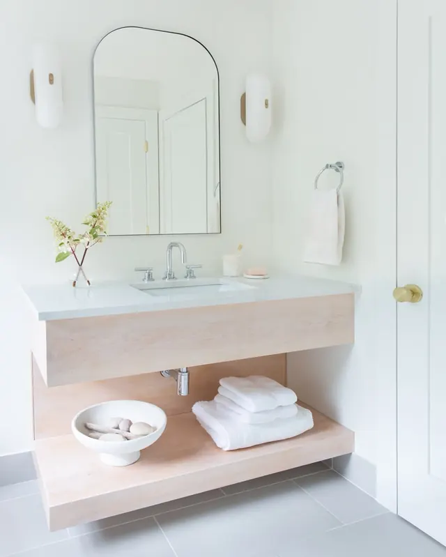 Bathroom with a floating maple vanity, open shelf, arched mirror and brass sconces