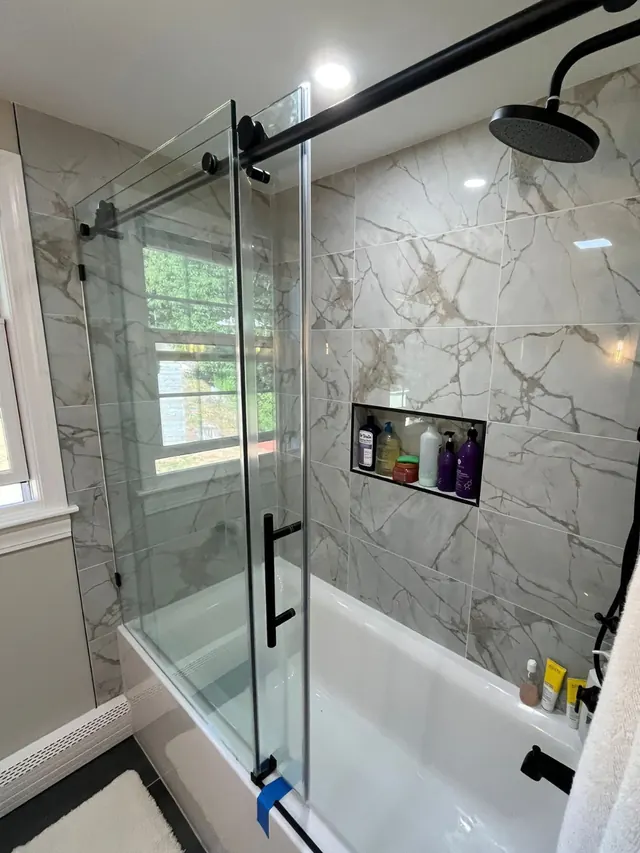 Tub and shower with marble-look tile, a sliding glass door and black fixtures