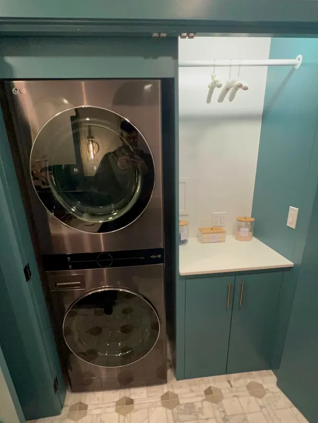 Laundry and bath after the remodel with green cabinets around a stacked washer and dryer