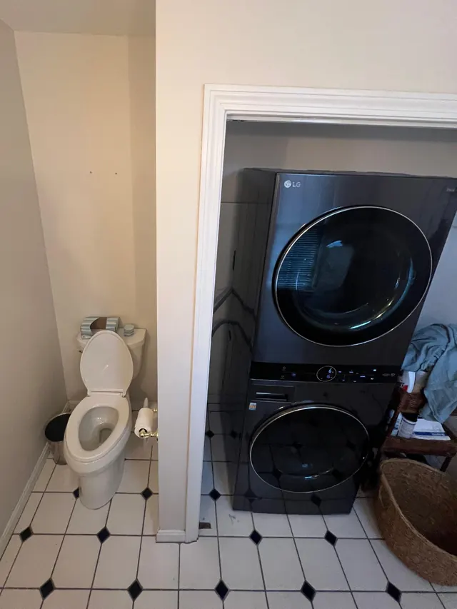Bathroom and laundry before the remodel with a toilet beside a stacked washer and dryer