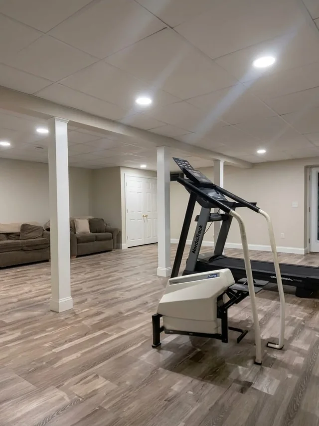 Finished basement with wood-look plank flooring, recessed lighting and a home gym area