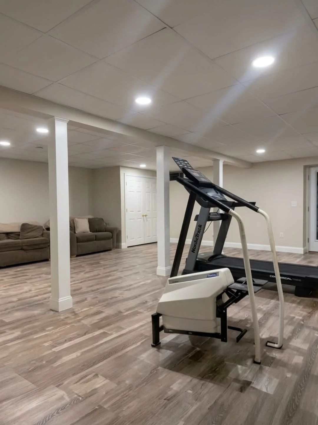 Finished basement with wood-look plank flooring, recessed lighting and a home gym area