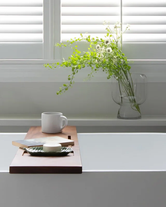 Freestanding soaking tub under a window with plantation shutters in a Central Massachusetts bathroom