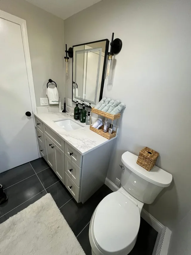 Remodeled bathroom with a gray vanity, black framed mirror and dark tile floor
