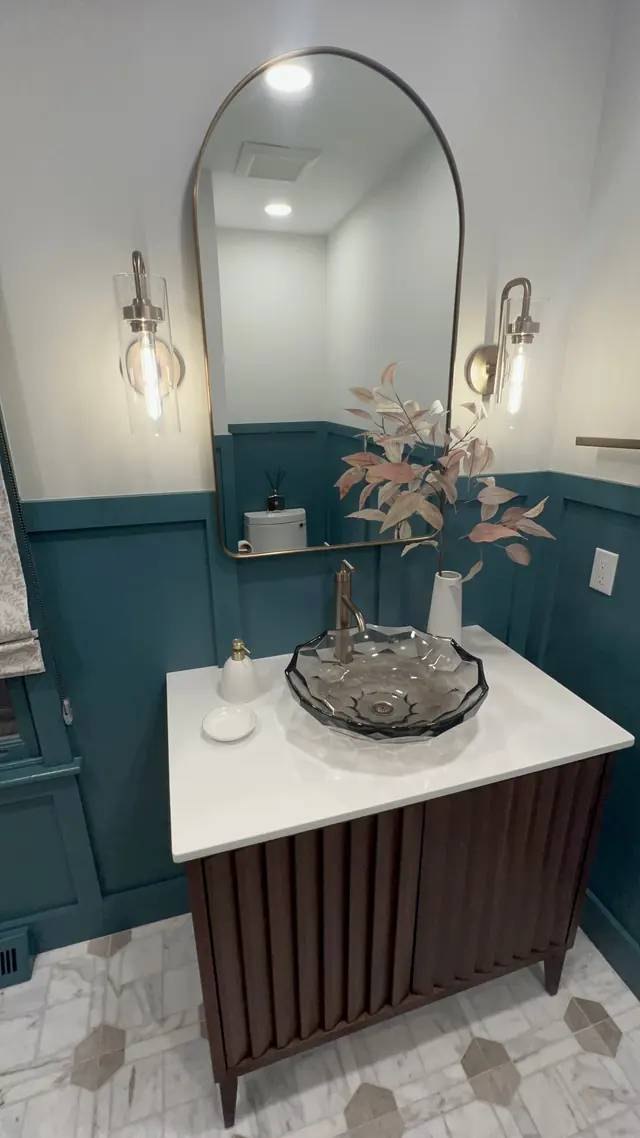 Teal powder room with wall paneling, a wood vanity and an arched mirror in Marlborough, MA, featured in New England Living