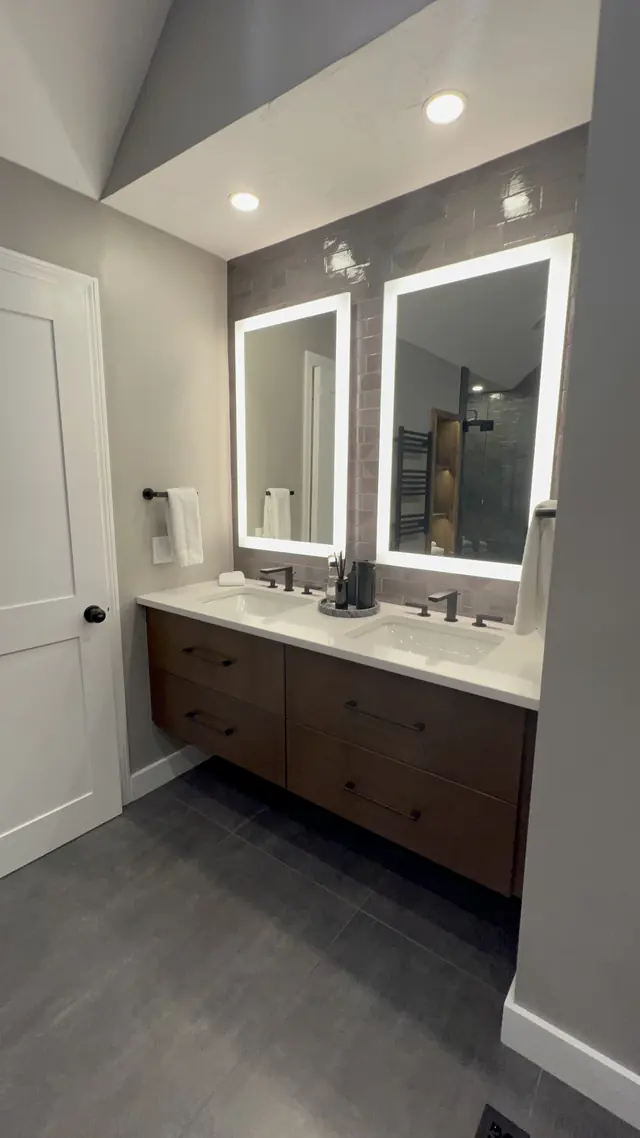 Wood double vanity with lighted mirrors after the primary bathroom remodel in Marlborough, MA