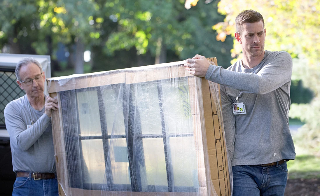 Two installers carrying a new window in protective packaging